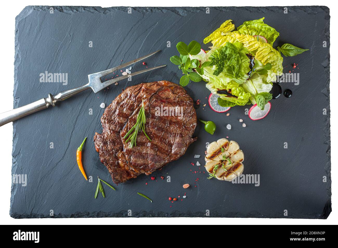 Una bistecca ribeye con un'insalata di rosmarino anh una lastra di pietra nera Foto Stock