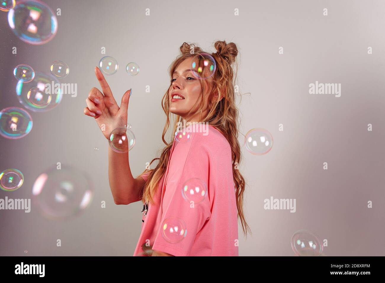 Abbastanza sorridente con i denti giovane ragazza europea. Capelli ondulati da surf. Ragazza con stile divertente capelli. Ragazza che indossa rosa t-corto, isolato su sfondo beige Foto Stock