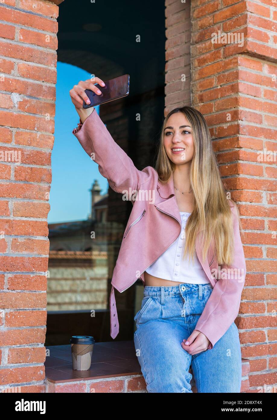 Ragazza bionda che guarda il suo telefono cellulare e che prende fuori i suoi selfie in attesa dei suoi amici Foto Stock