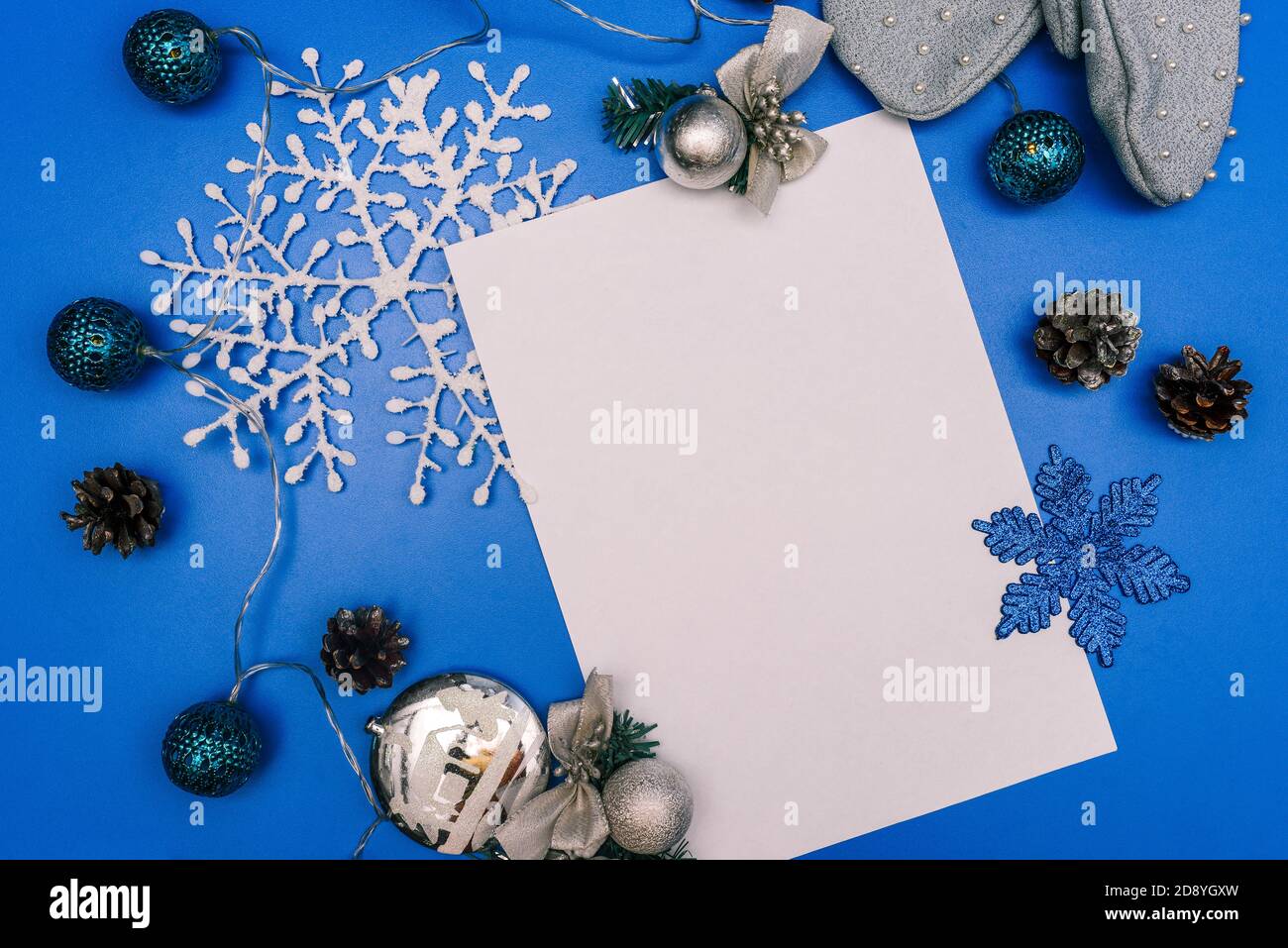 Composizione di Natale. Fiocco di neve di carta, ghirlanda, foglio di carta e guanti invernali su sfondo blu. Concetto di anno nuovo con spazio di copia Foto Stock