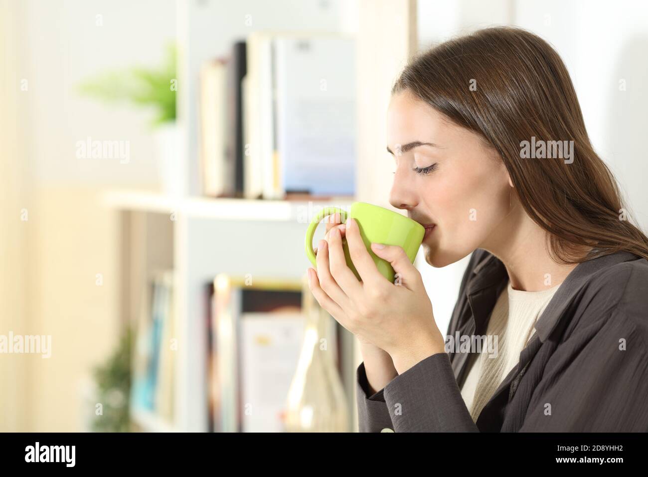 Profilo di una donna che beve caffè dalla tazza in piedi dentro il soggiorno a casa Foto Stock