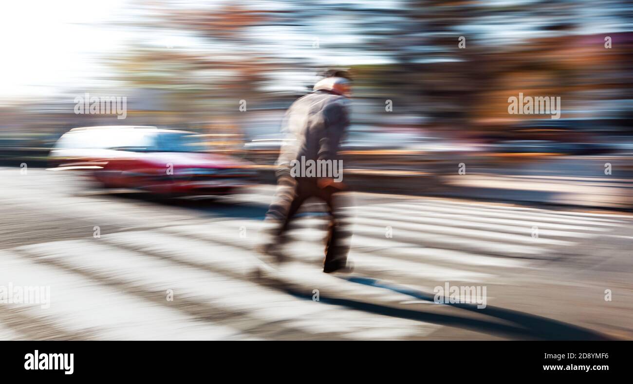 Situazione pericolosa in caso di attraversamento della zebra. Un uomo anziano attraversa la strada di fronte all'auto. Sfocatura intenzionale del movimento. Foto Stock