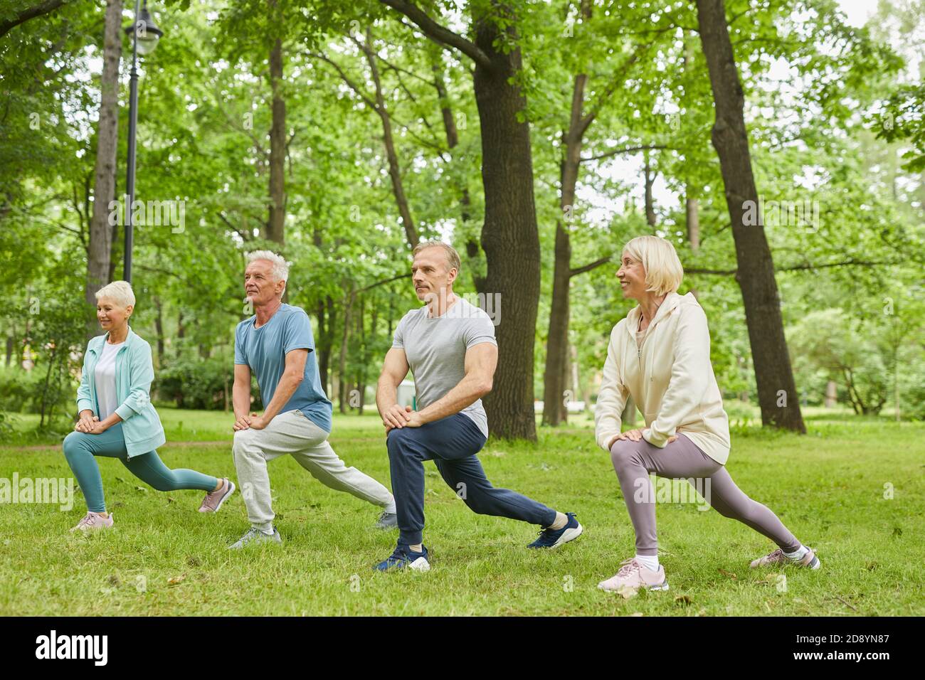 Gruppo di quattro uomini e donne senior che indossano abiti sportivi esercizio di allungamento delle gambe in parcheggio Foto Stock