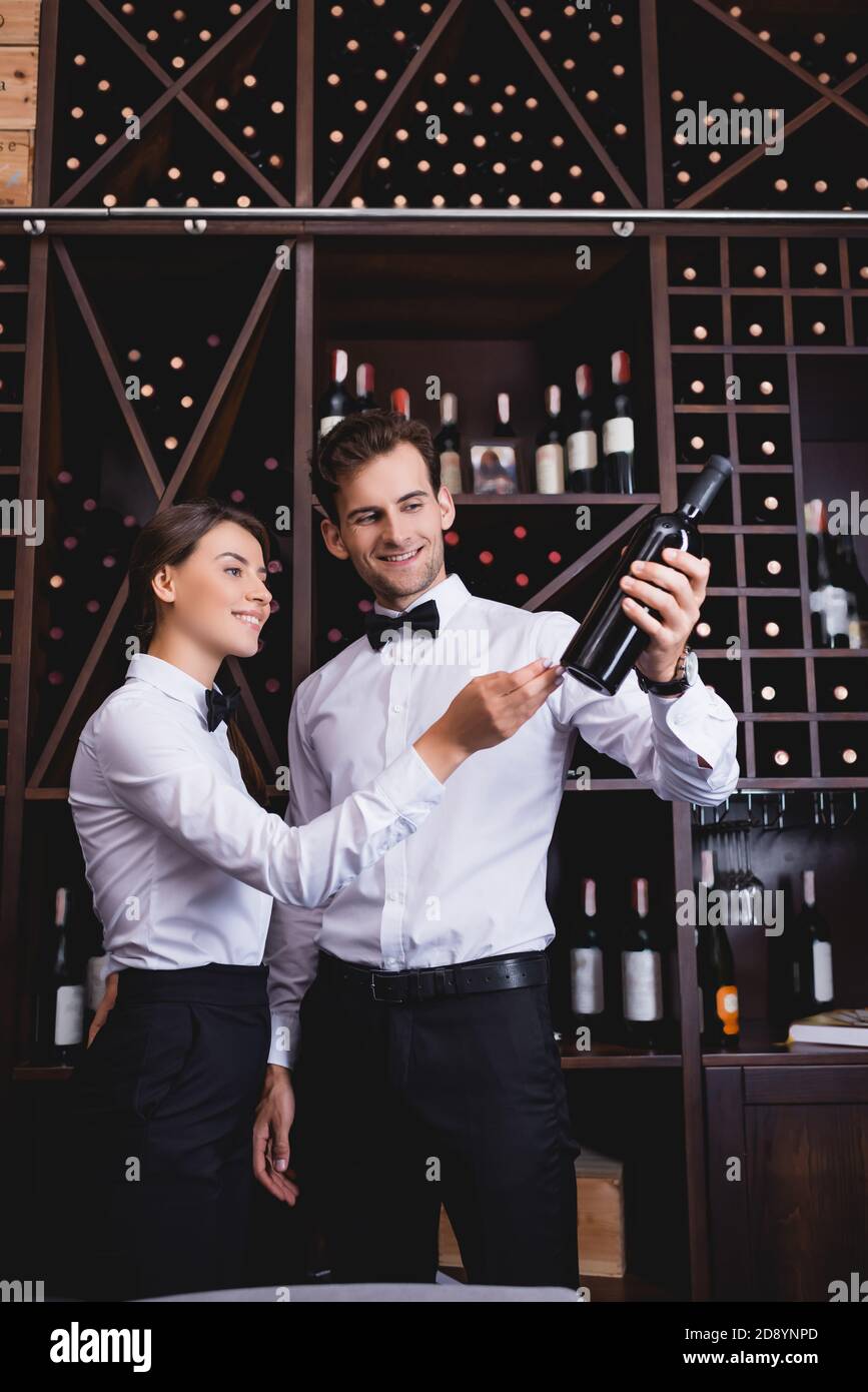 Fuoco selettivo del sommelier che punta con la mano alla bottiglia di vino vicino a un collega nel ristorante Foto Stock