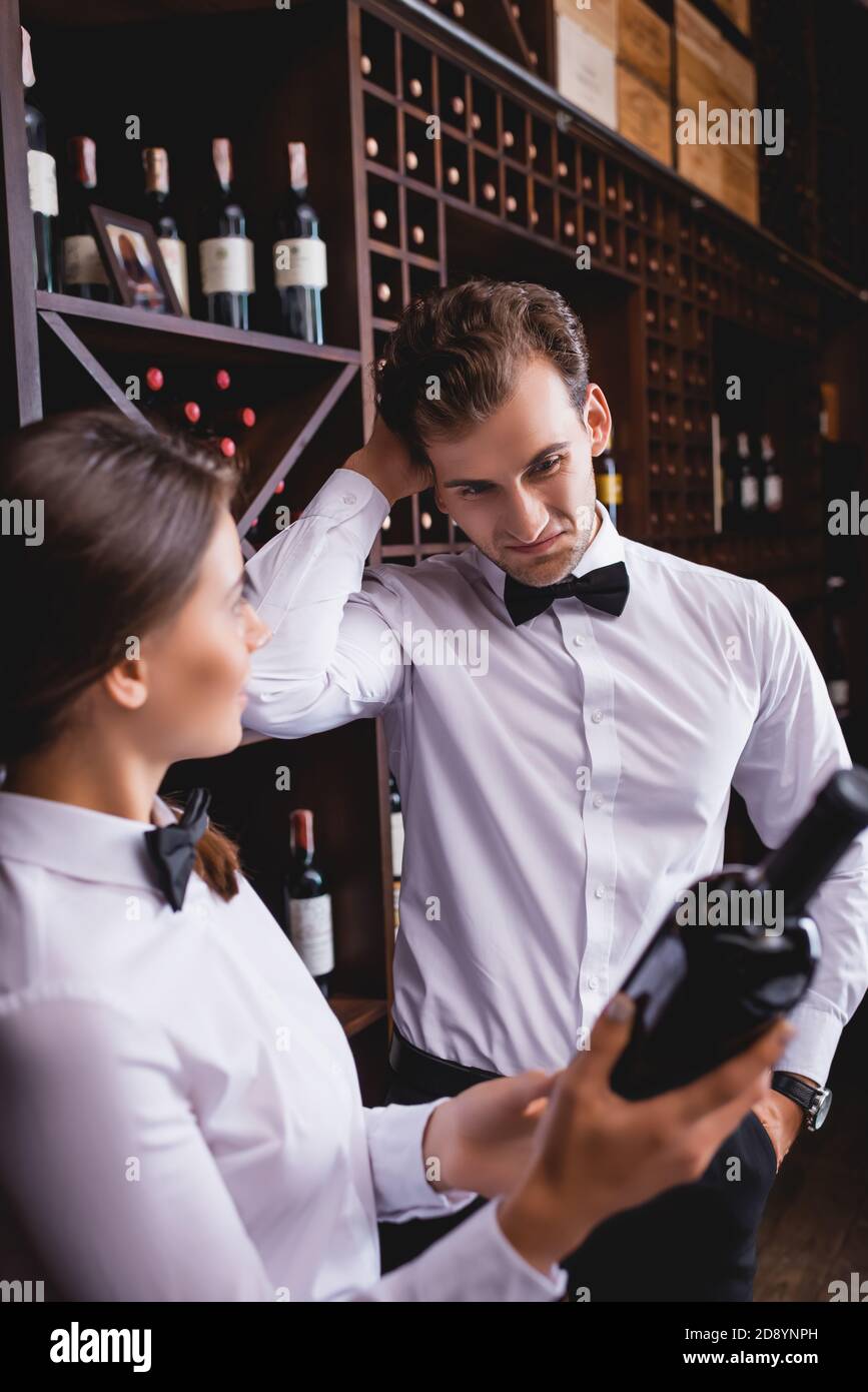 Fuoco selettivo del sommelier pensivo con mano in tasca in piedi vicino collega con bottiglia di vino Foto Stock