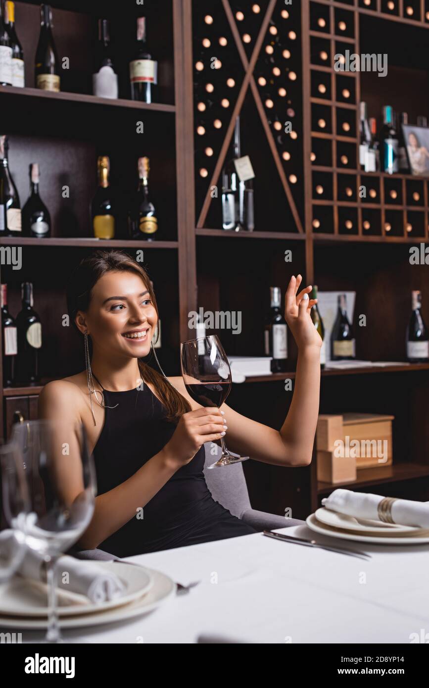 Fuoco selettivo della giovane donna che agita la mano mentre tiene il vetro di vino nel ristorante Foto Stock