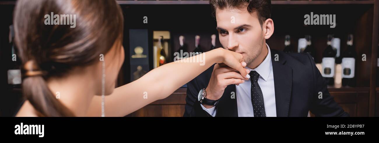 Raccolto panoramico di uomo elegante baciando mano di ragazza dentro ristorante Foto Stock