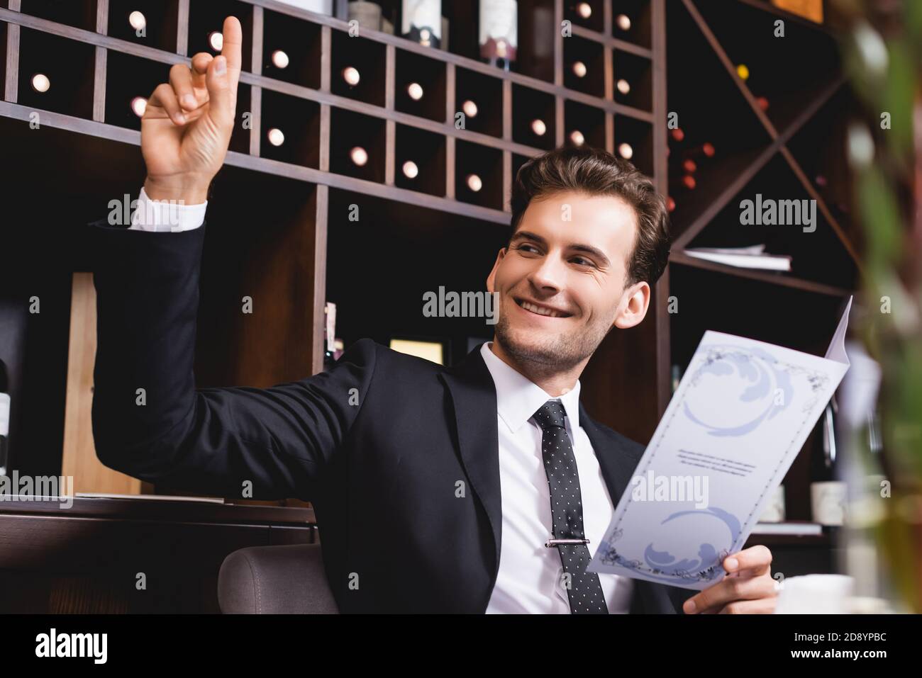 Fuoco selettivo dell'uomo in tuta con la mano rialzata che guarda lontano in ristorante Foto Stock