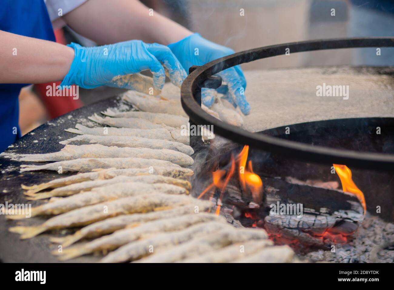 Chef cucina a mano europeo odore di pesce in farina su braciere nero in estate mercato alimentare all'aperto: Primo piano. Frutti di mare, barbecue, gastronomia, cucina Foto Stock