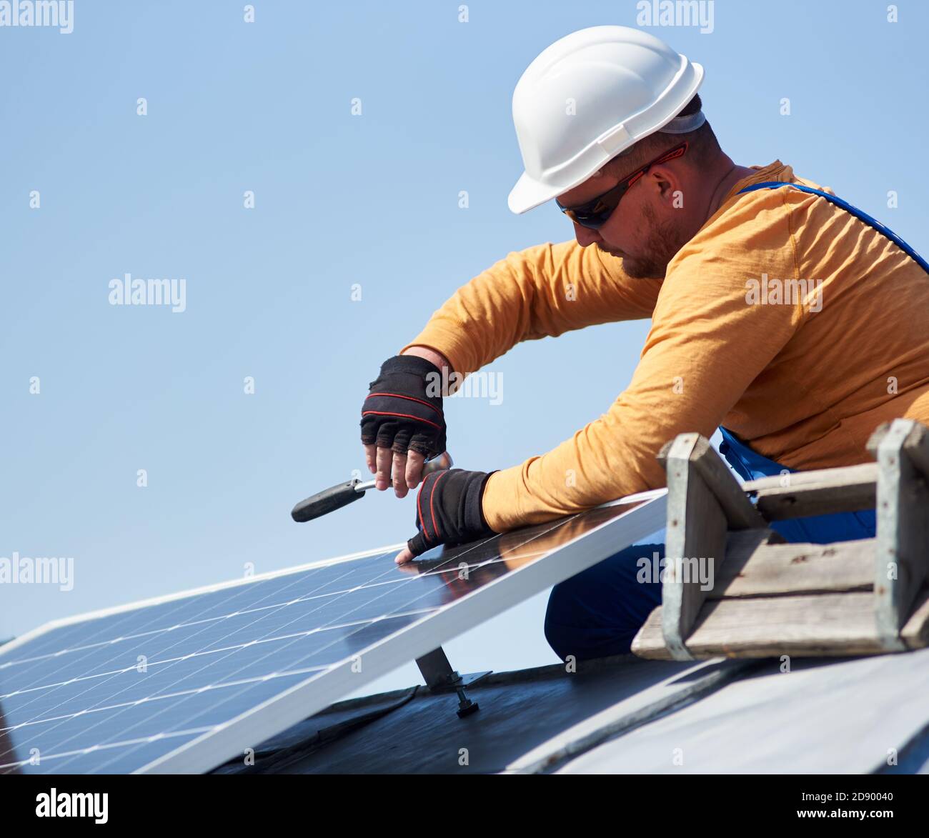 Uomo ingegnere in casco di protezione che installa un sistema autonomo di pannelli fotovoltaici solari con vite. Elettricista che monta il modulo solare sul tetto della casa moderna. Concetto ecologico di energia alternativa. Foto Stock