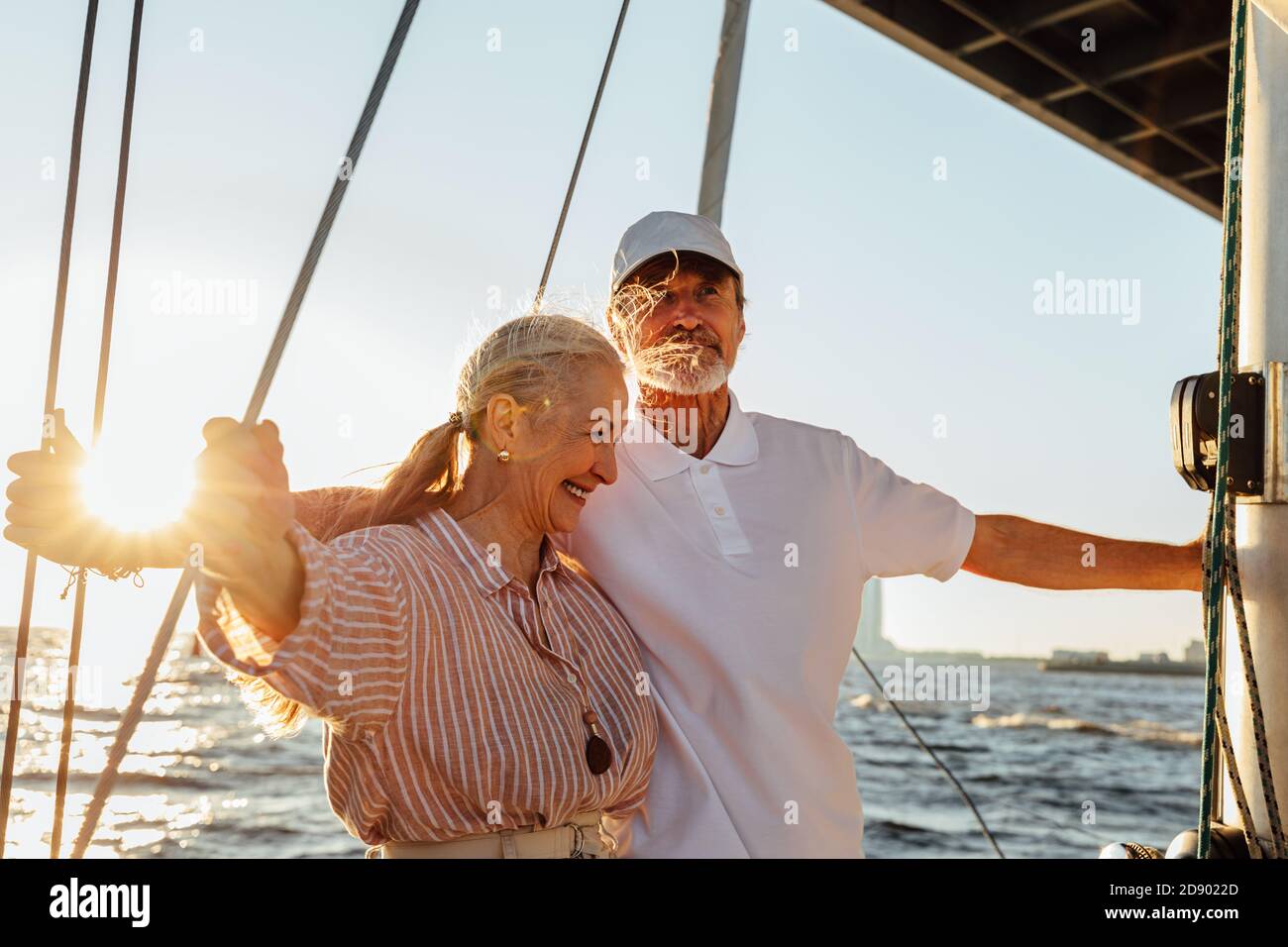 Coppie anziane che si godono la loro vacanza su uno yacht privato. Due persone anziane che si levano in piedi insieme su una barca a vela al tramonto. Foto Stock