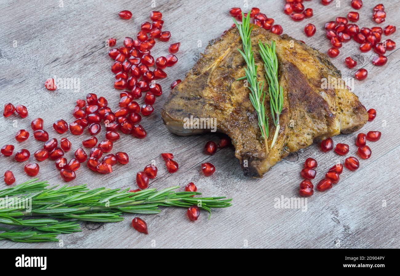 bistecca alla griglia su fondo ligneo. pezzo di carne fritta con semi di melograno e un rametto di rosmarino. Foto Stock