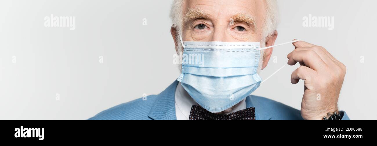 Uomo anziano che tiene la maschera medica isolata su grigio, striscione Foto Stock