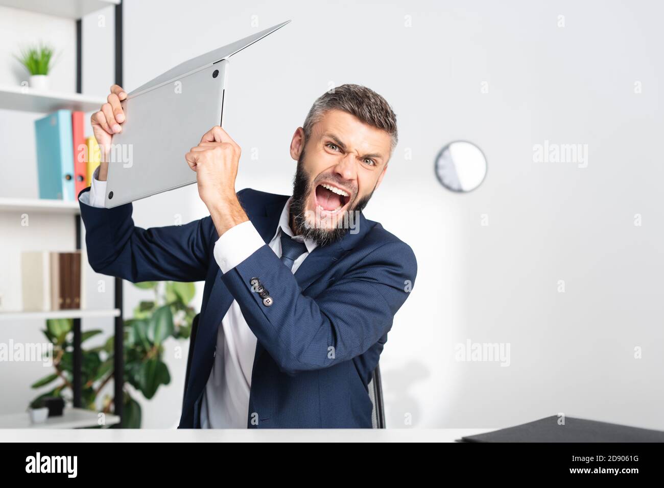 Uomo d'affari arrabbiato urlando mentre tiene il laptop in ufficio Foto Stock