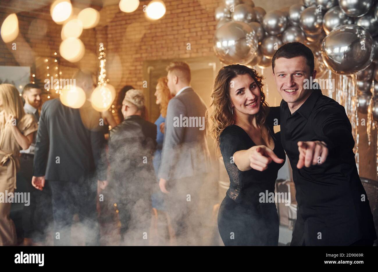 Giovane coppia in piedi insieme contro i loro amici in natale decorato e festeggiando il nuovo anno Foto Stock