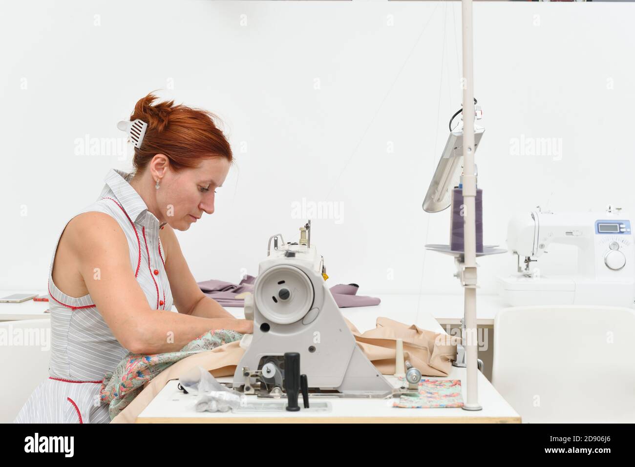 La donna di età media lavora ad una macchina da cucire in un laboratorio di cucito Foto Stock