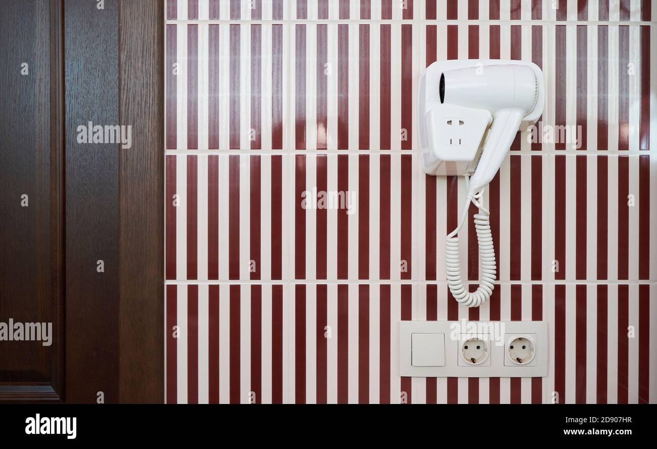 Un asciugacapelli bianco appeso su una parete piastrellata in un bagno Foto Stock