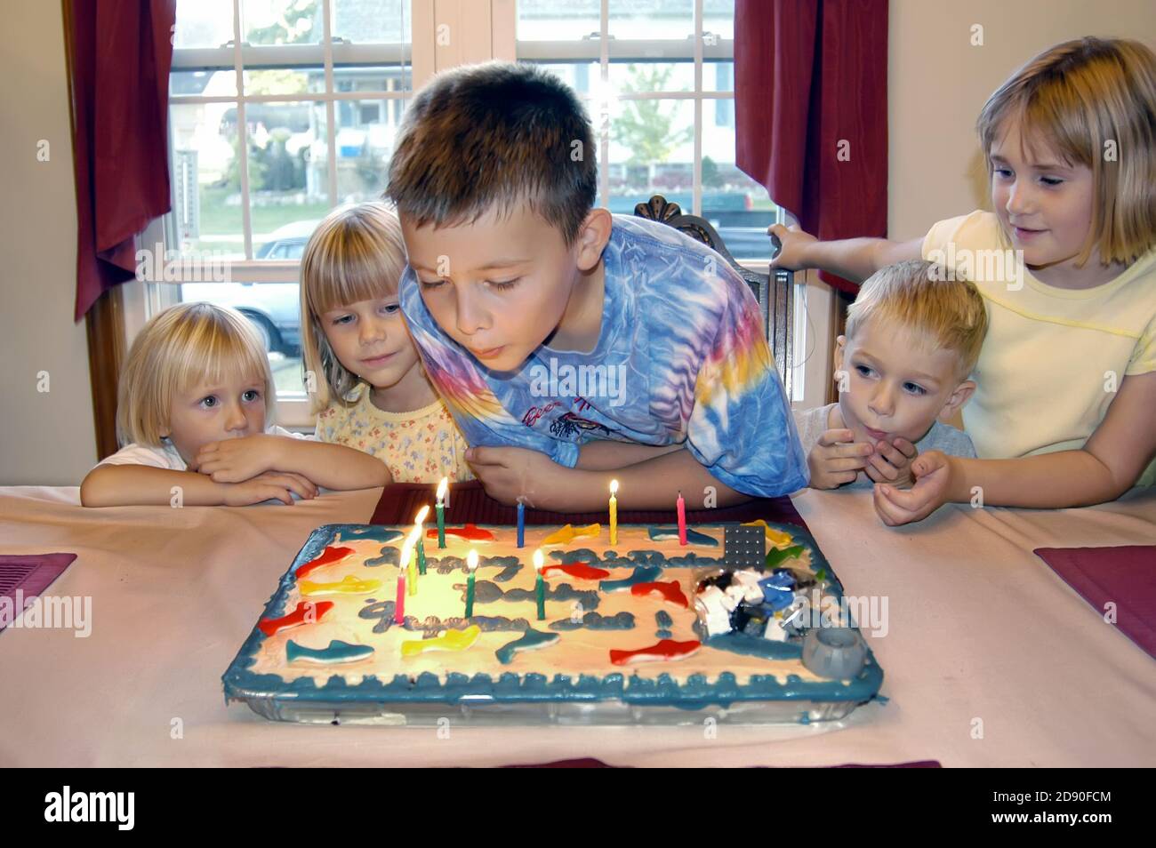 il ragazzo di 9 anni festeggia il compleanno con gli amici condividendo i regali e una torta con le candele Foto Stock