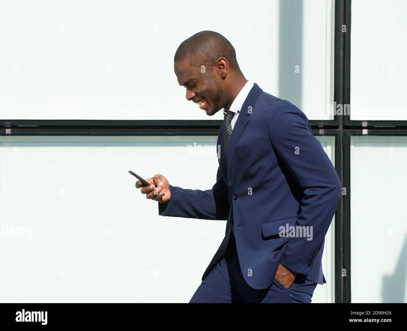 Ritratto laterale di felice uomo d'affari afroamericano che cammina con cellulare in città Foto Stock