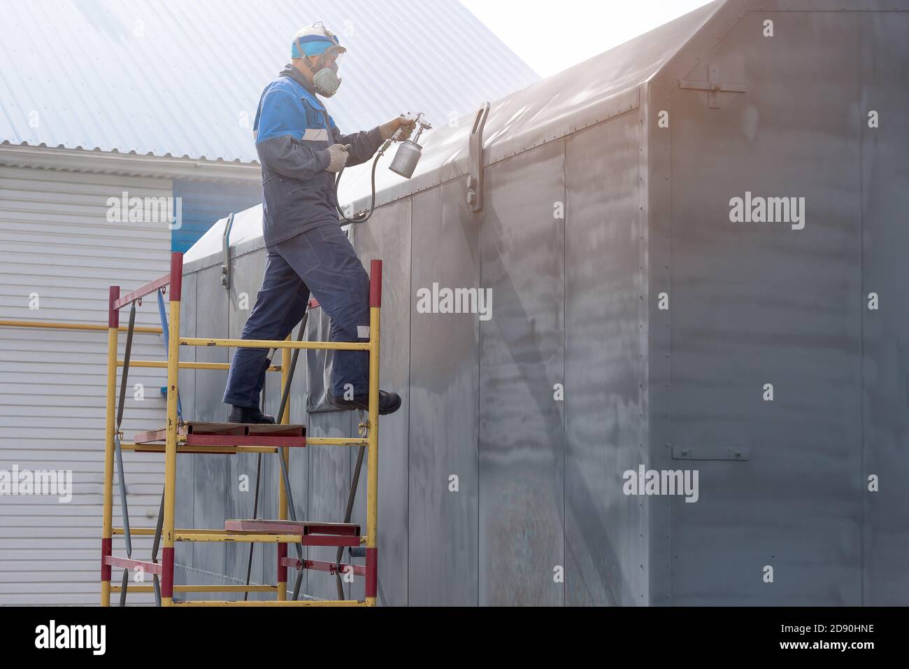 Lavoro industriale. Adescamento di prodotti metallici dalla pistola di compressione. Un operatore in tute e un respiratore dipinge il corpo di un rimorchio o di un Foto Stock