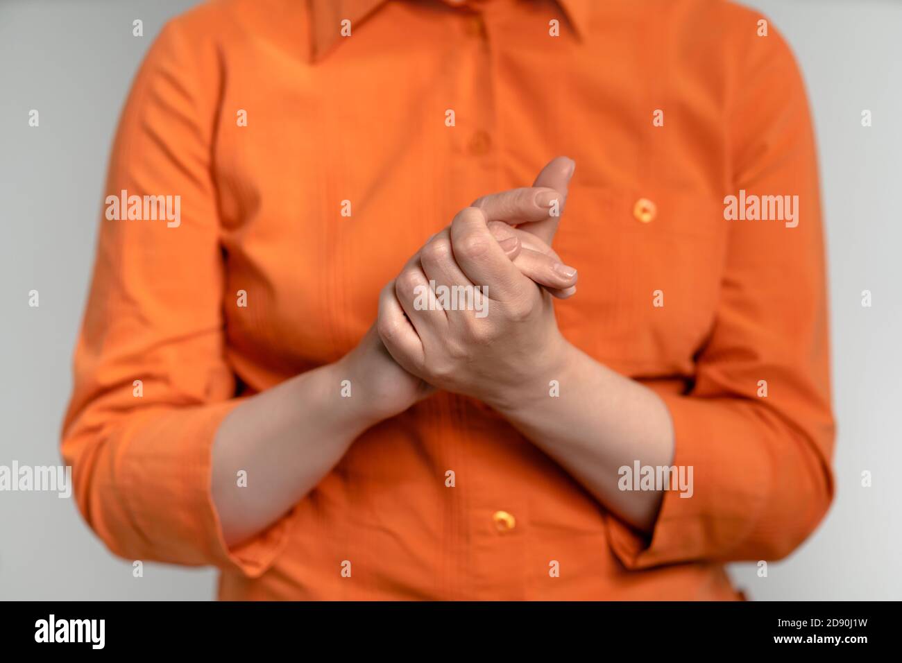 Donna matura in camicia arancione ha piegato le mani. Donna unita alle mani. Primo piano. Isolato su sfondo bianco. Vista frontale Foto Stock