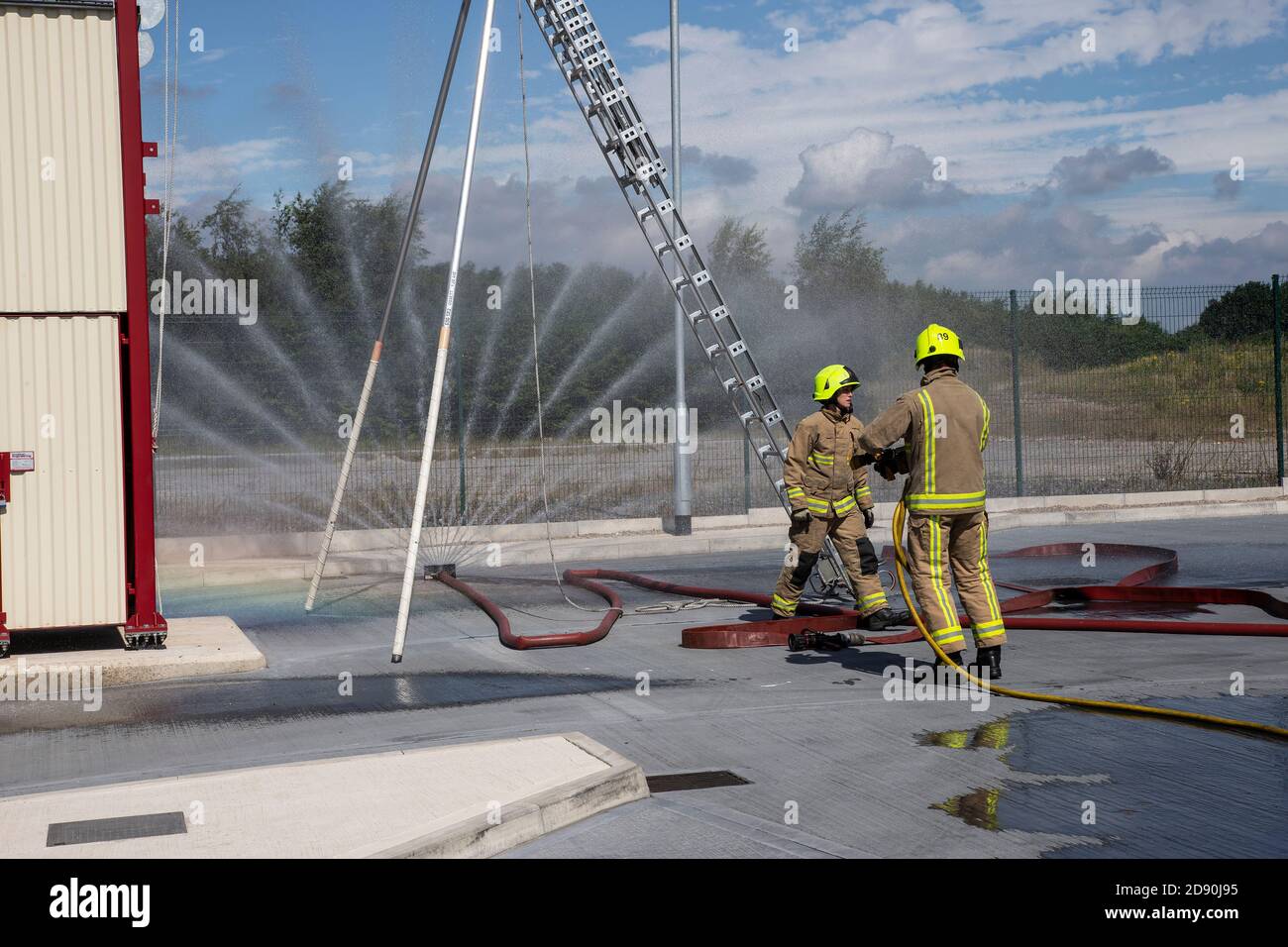 Due vigili del fuoco inglesi in equipaggiamento di protezione completo che controlla il funzionamento Di una manichetta antincendio alla stazione dei vigili del fuoco di Ossett a Wakefield West Yorkshire Inghilterra Foto Stock