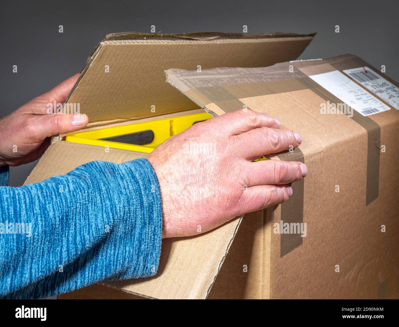 Primo piano POV di un uomo che tiene le alette del coperchio di una scatola di cartone appena aperta per la spedizione. Foto Stock