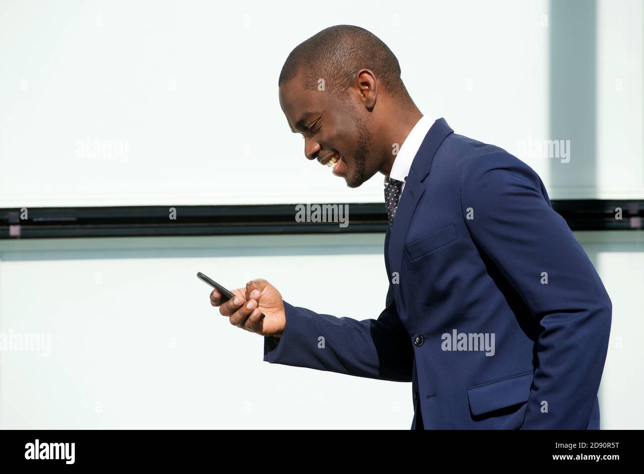 Ritratto laterale di sorridente uomo d'affari afroamericano che cammina con cellulare in città Foto Stock