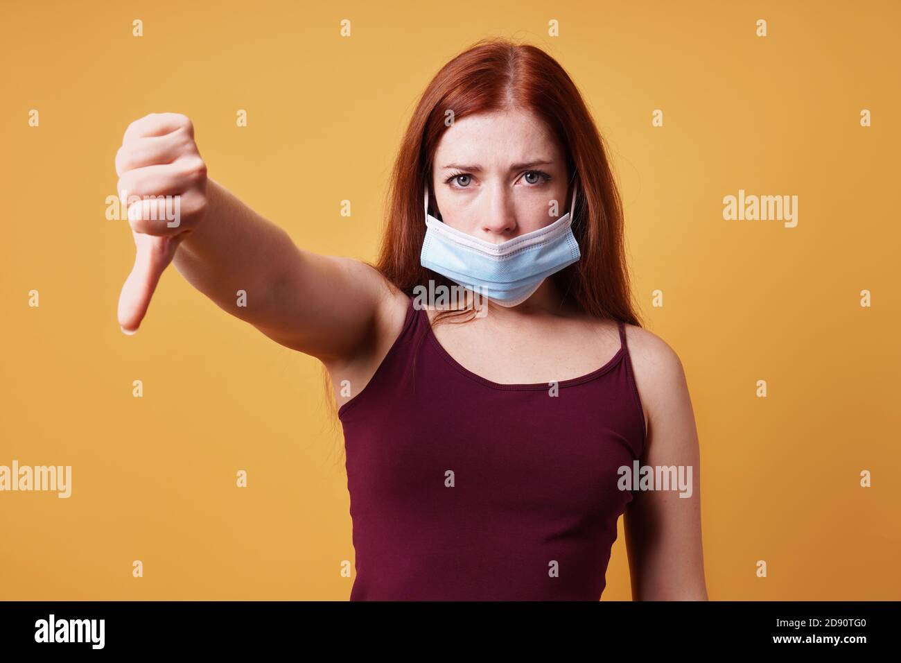 giovane donna che indossa una maschera medica errata sotto il naso e. fare i pollici verso il basso gesto - protesta contro la corona virus covid misure Foto Stock