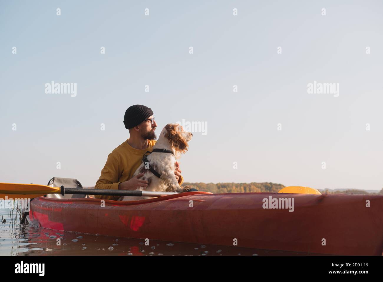 Kayak con cani: L'uomo si siede in una barca a remi sul lago accanto al suo spaniel. Riposo attivo e avventure con gli animali domestici, a cavallo di una canoa con il cane Foto Stock