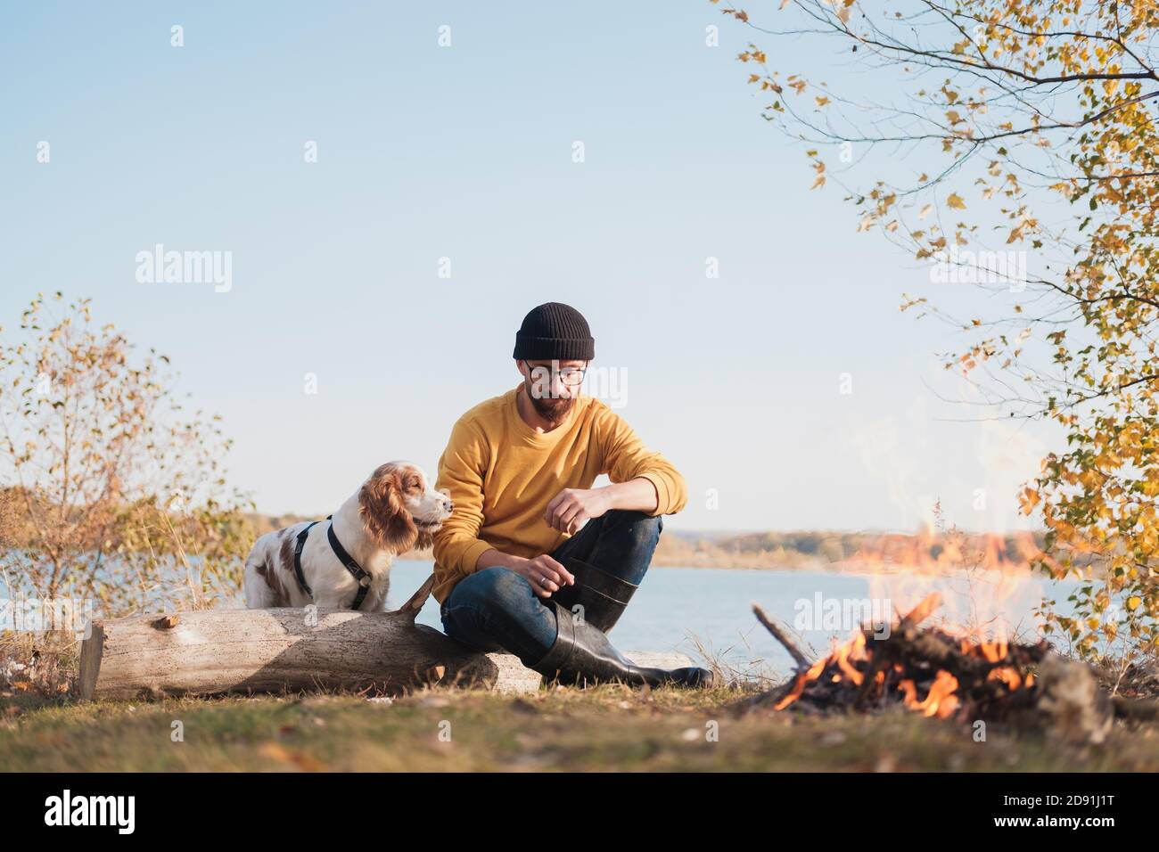 L'uomo abbraccia il suo cane seduto accanto al lago. Riposo attivo con animali domestici, avventure in corso, compagnia: cane spagnolo e il suo proprietario si siedono all'aperto Foto Stock