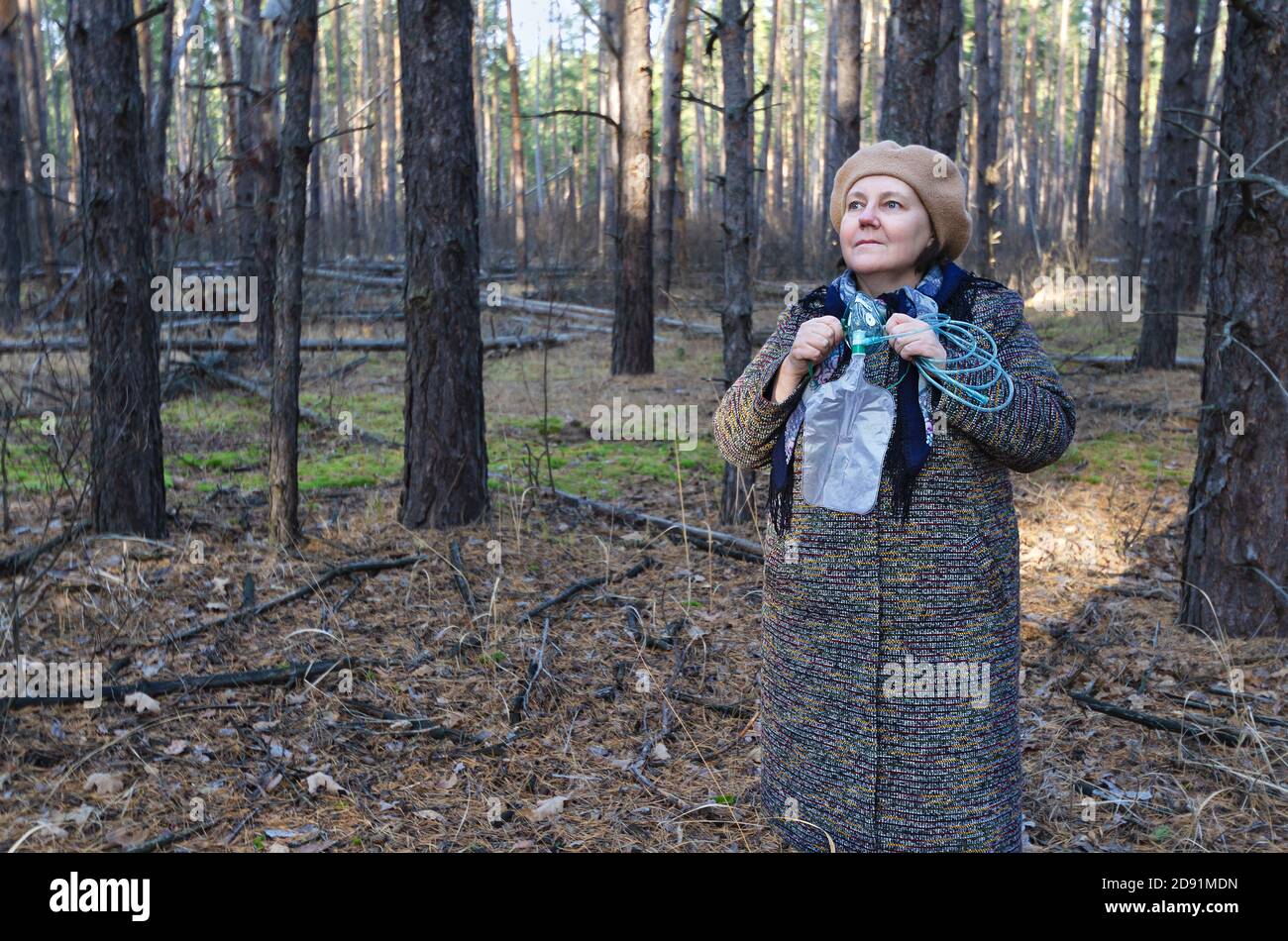 Una donna anziana nei boschi con una maschera di ossigeno nelle mani. Il concetto di aria forestale rispetto all'ossigeno in una maschera Foto Stock