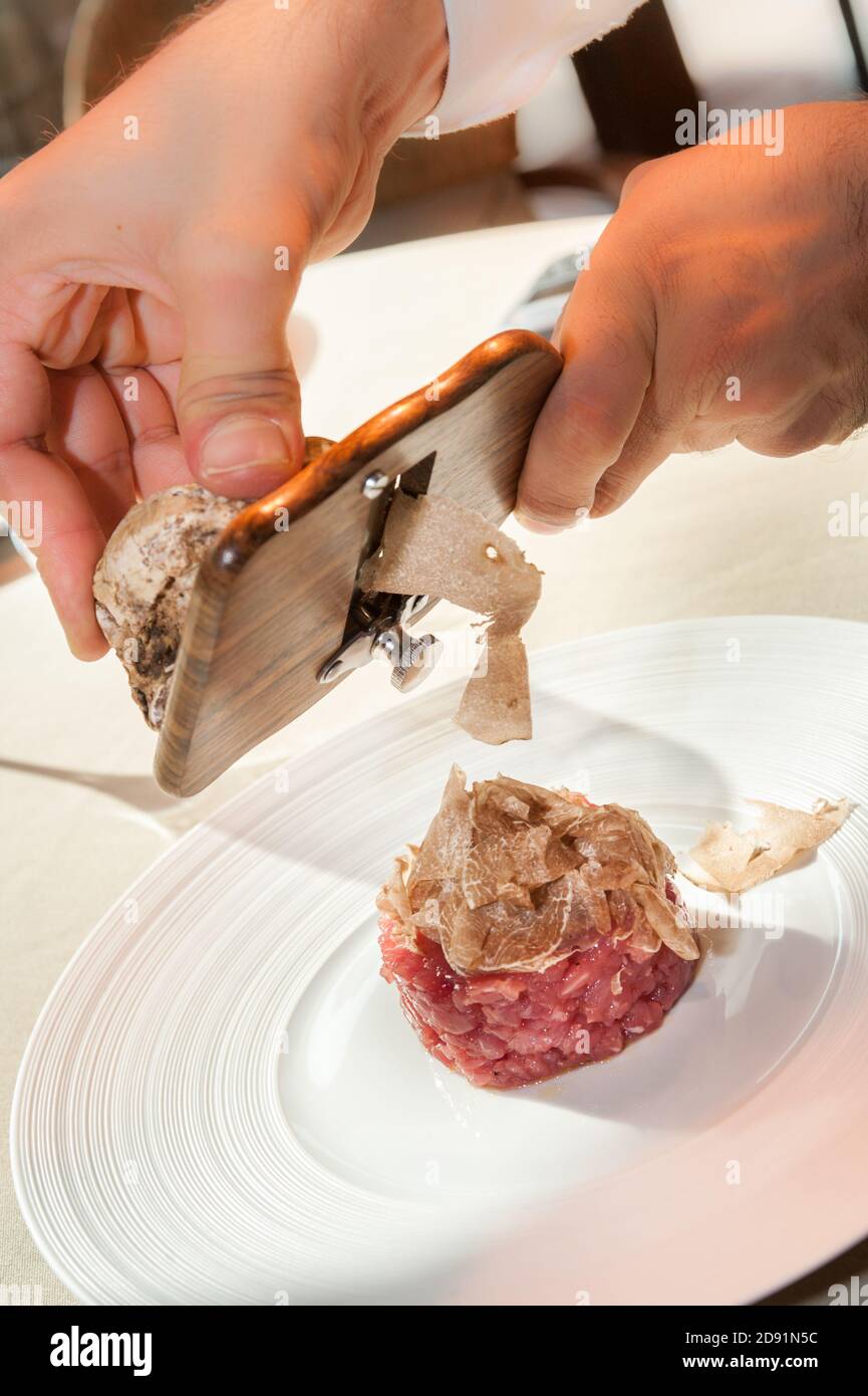 Tartufo bianco di Alba affettato dalle mani del cameriere su crudo Carne tritata di manzo piemontese di razza Fassona Foto Stock