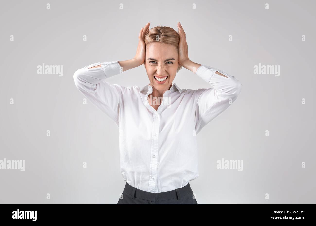 Stressato dipendente d'ufficio che si aggrappava la testa, sentendosi arrabbiato o disperato su sfondo grigio chiaro studio Foto Stock