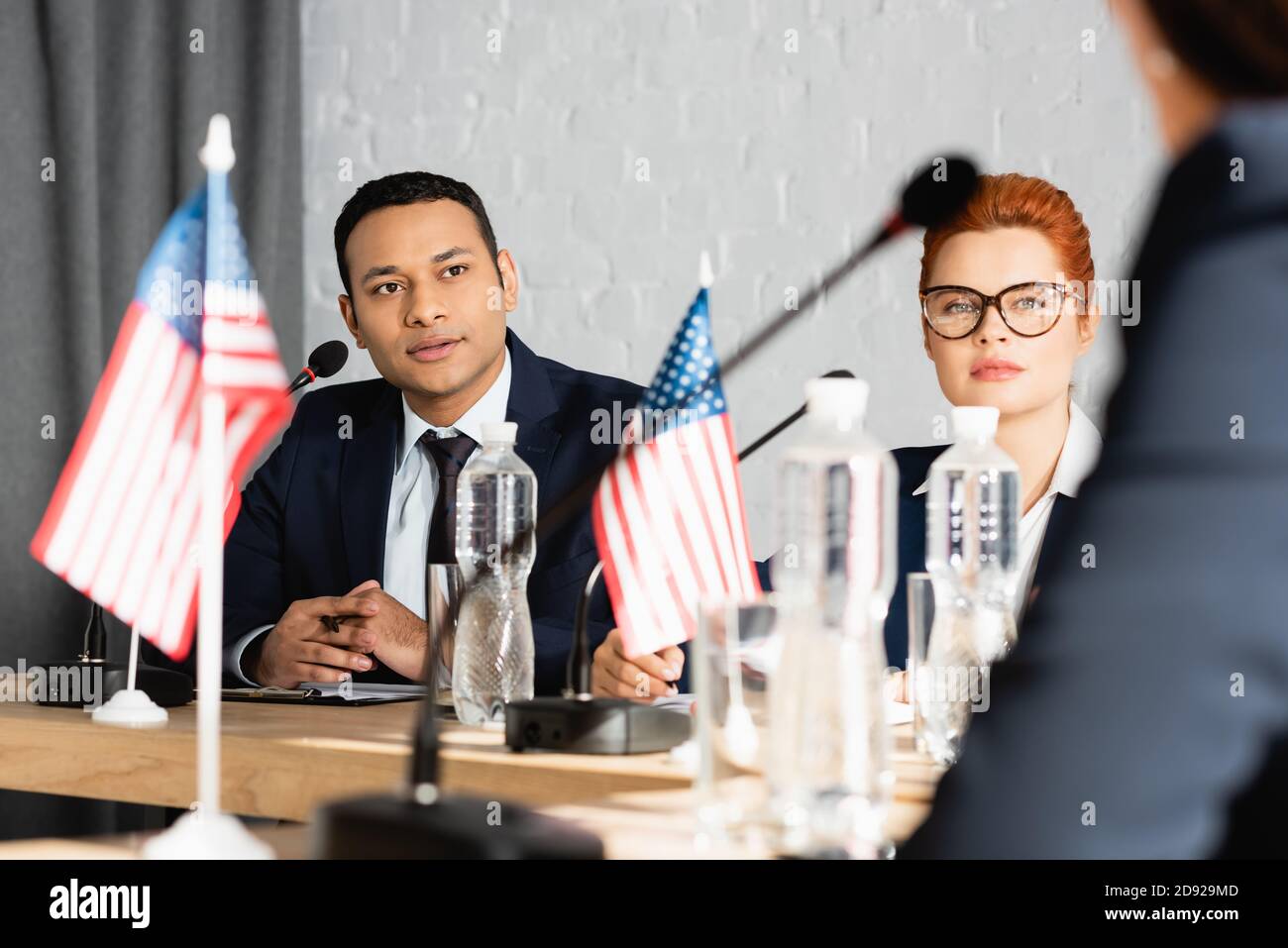 Politici interrazziali focalizzati che guardano la collega femminile mentre si siedono dentro sala riunioni in primo piano sfocato Foto Stock