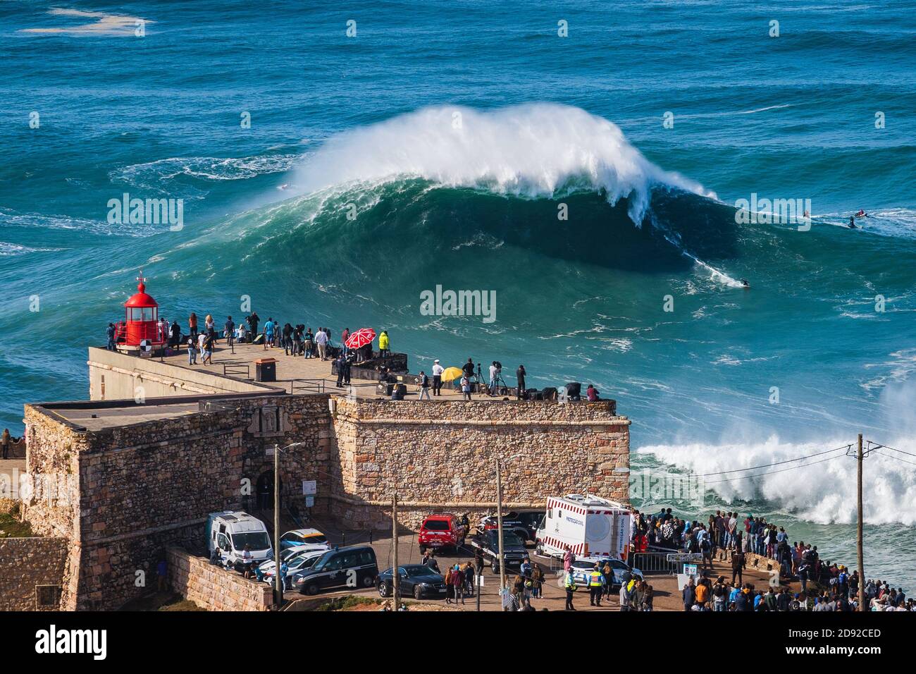 Surfista che cavalcano un'enorme onda vicino al faro di Nazare, Portogallo. Nazare è noto ai surfisti per avere le onde più grandi del mondo. Foto Stock