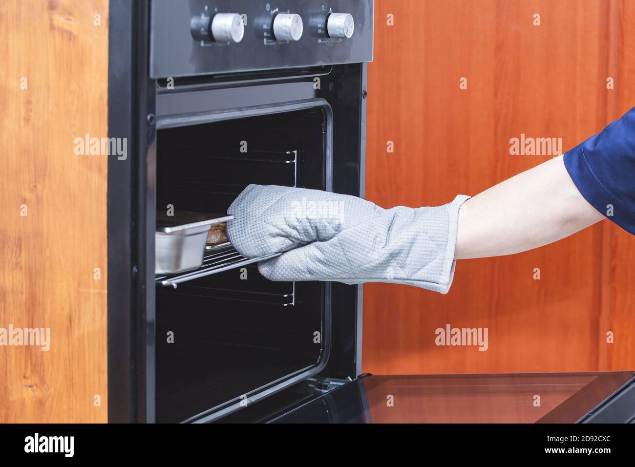 Una mano in un guanto protettivo tira fuori un piatto di carne calda cotta dal forno. Concetto di sicurezza. Cucina, preparazione del cibo, cucina. Ristorante, caffè, mangiare Foto Stock