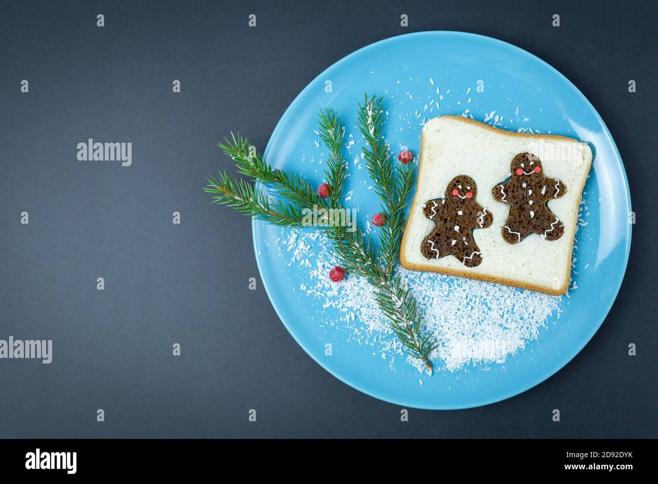 Pane tostato, decorato con pan di zenzero glaze, ribes rosso congelato, ramo di abete rosso su un piatto blu, su uno sfondo scuro. Natale, anno nuovo. Fest Foto Stock