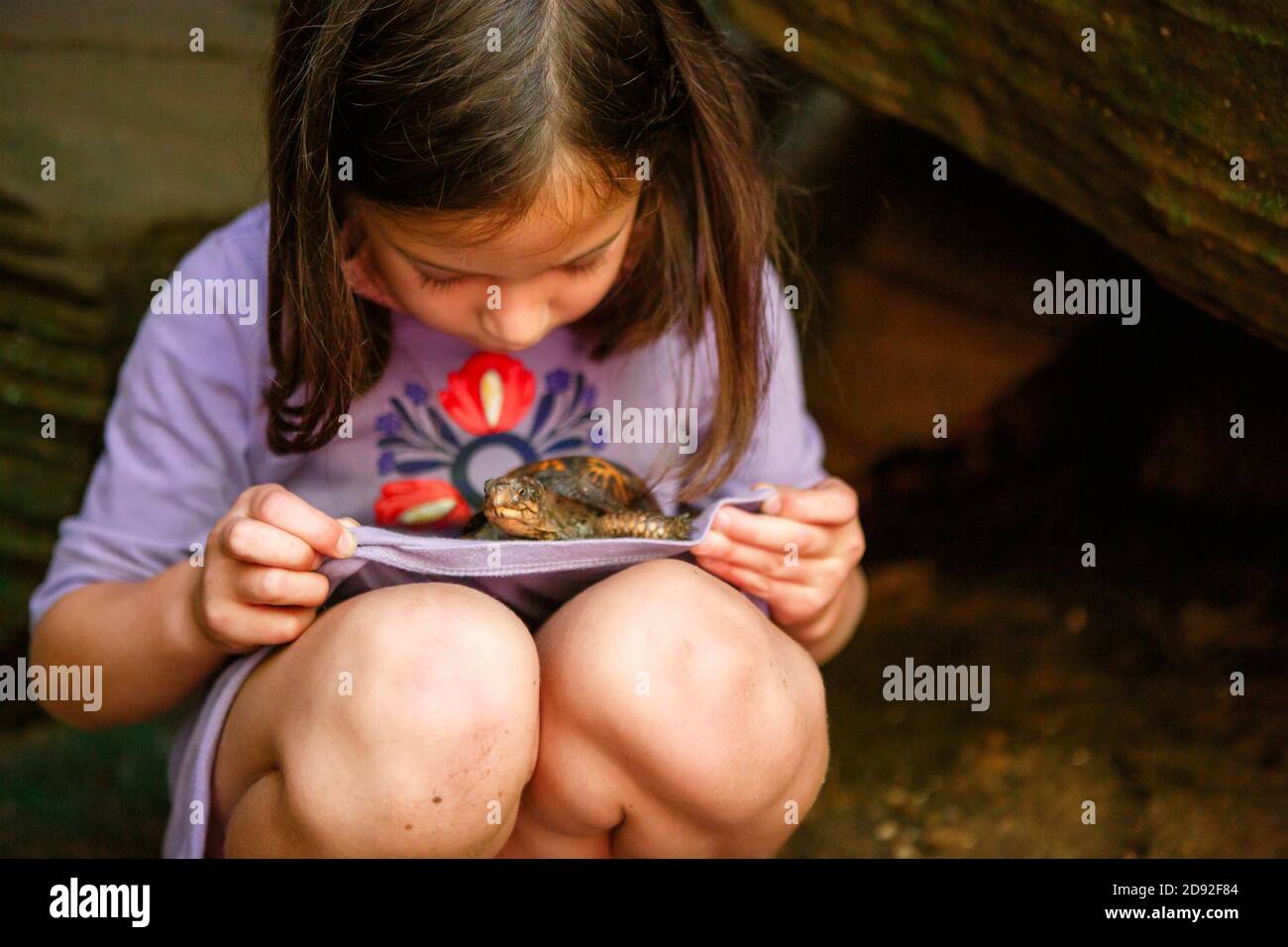 Una bambina con le ginocchia sporche tiene una piccola tartaruga in grembo Foto Stock