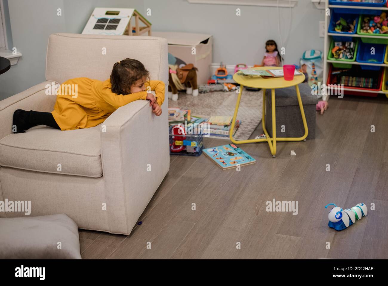 bambina che si stesa sulla sedia e guarda un giocattolo Foto Stock