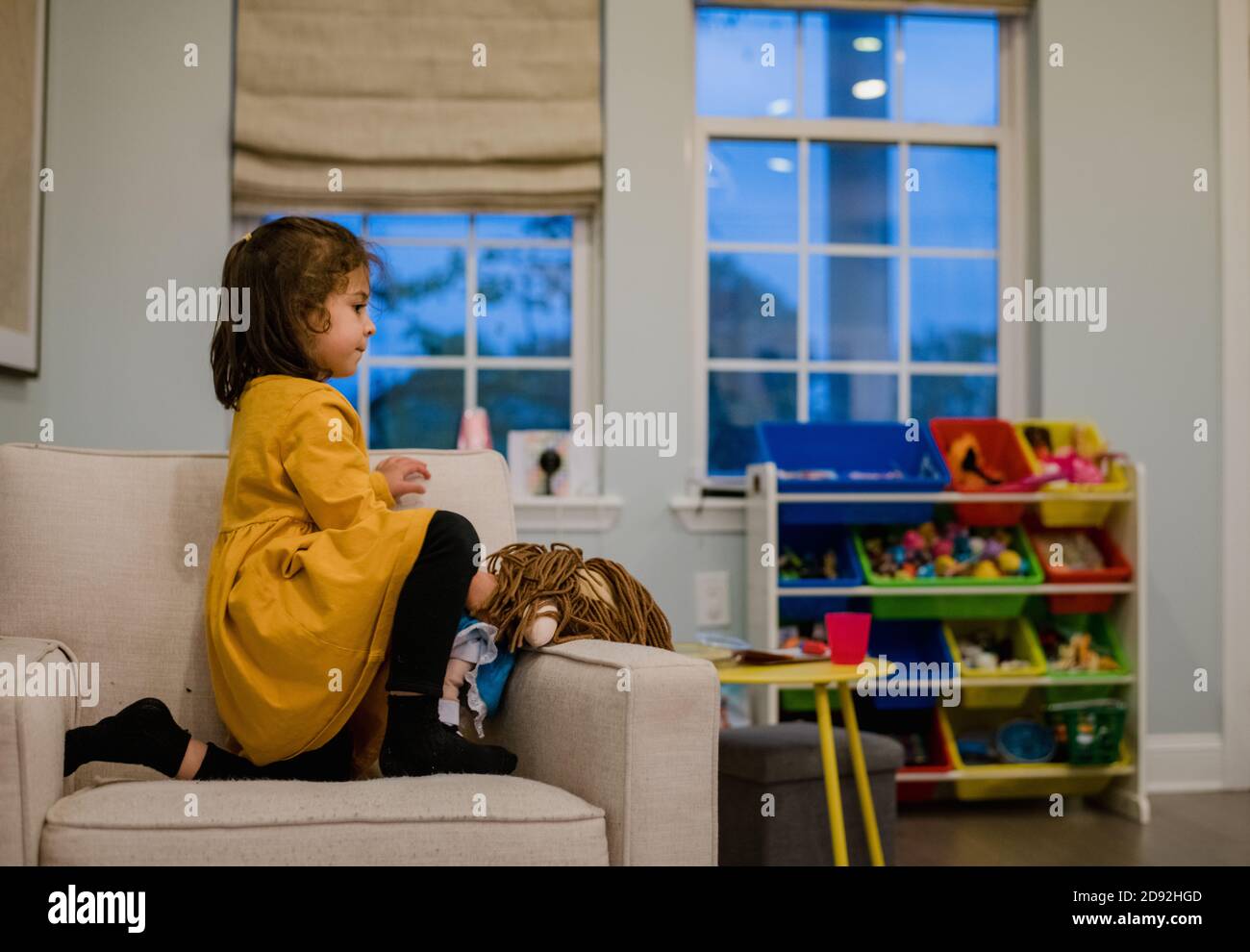 ragazza prescolare inginocchiata su una sedia in una colorata sala giochi Foto Stock