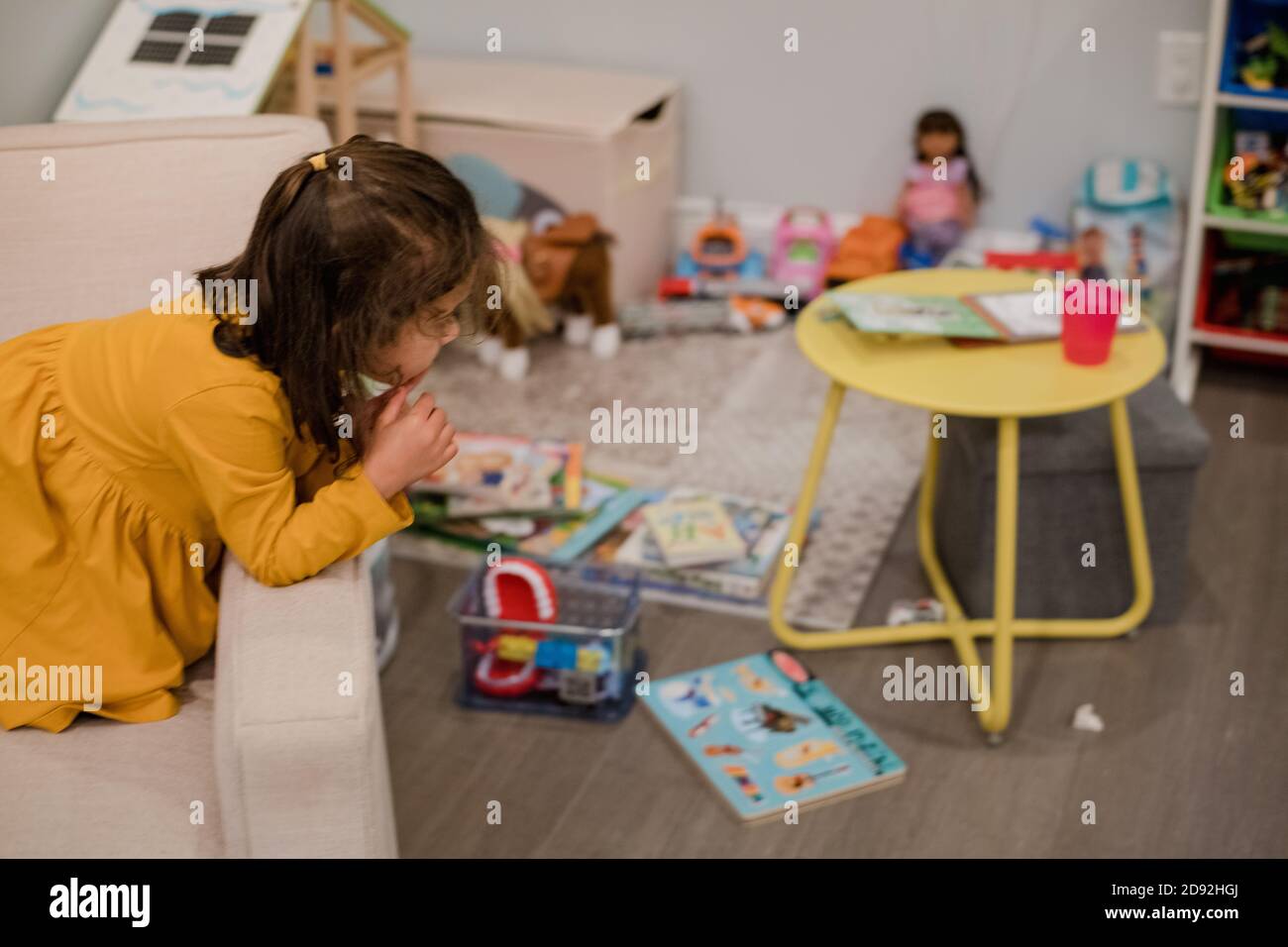 età prescolare ragazza che guarda i giocattoli della sala da gioco da una sedia Foto Stock