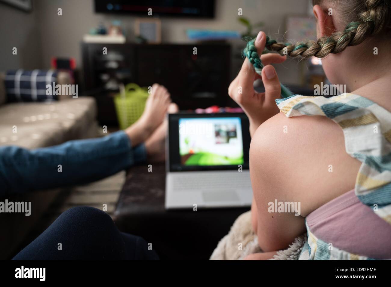 Tween Girl giocare con i capelli mentre si guarda il laptop in Soggiorno Foto Stock