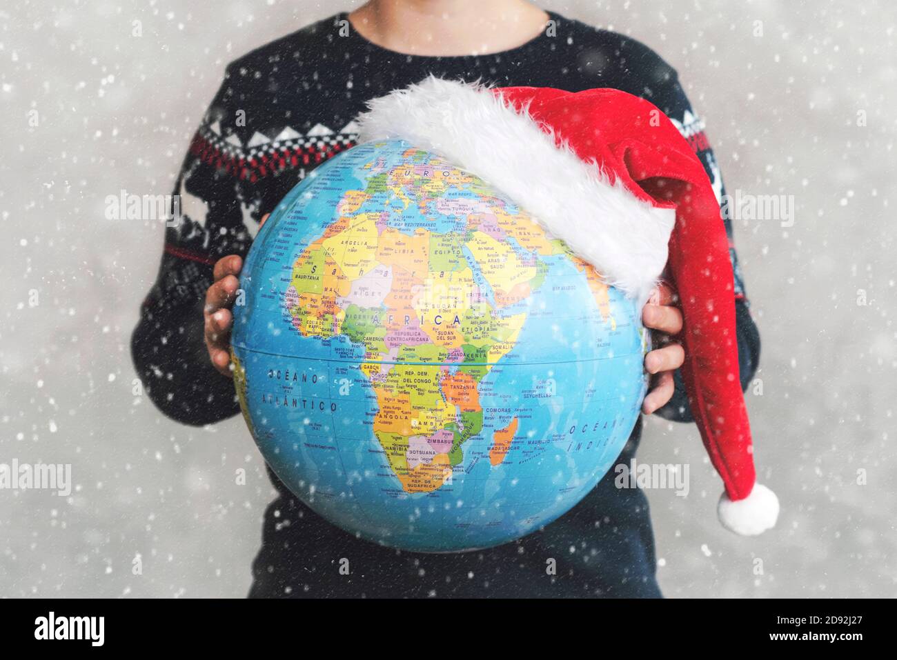 Buon Natale. capretto che tiene il globo della terra con un cappello di Santa con i fiocchi di neve Foto Stock