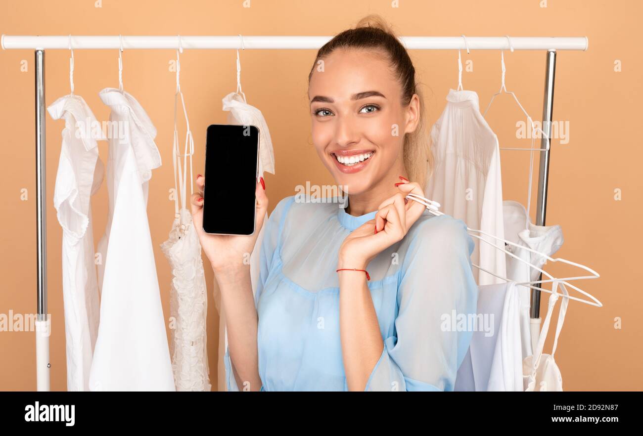 Donna sorridente che mostra lo schermo nero del telefono e gli appendiabiti Foto Stock