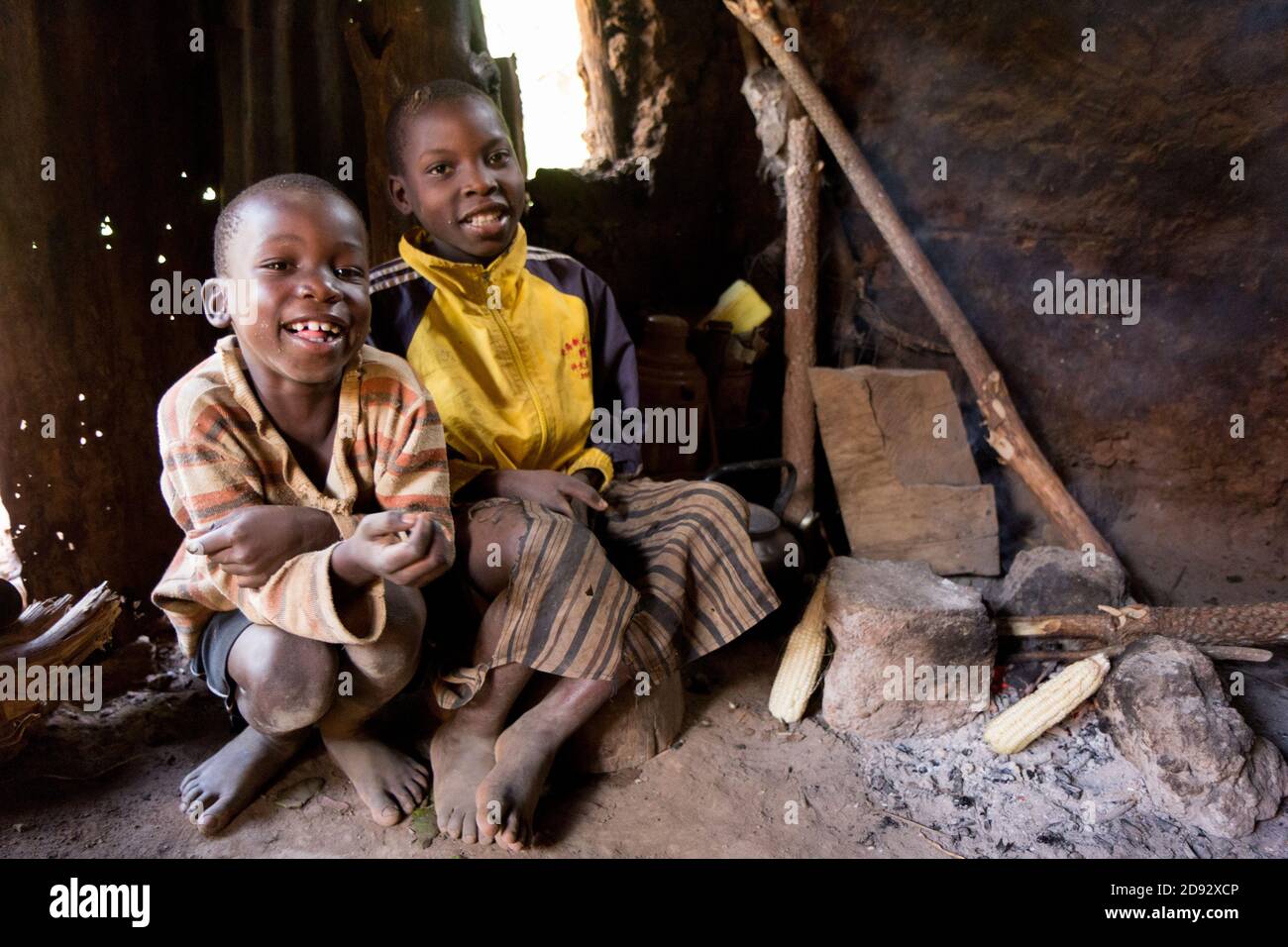 Due ragazzi seduti a un fuoco/brace in una casa di sonaglino nella campagna ugandese. Foto Stock