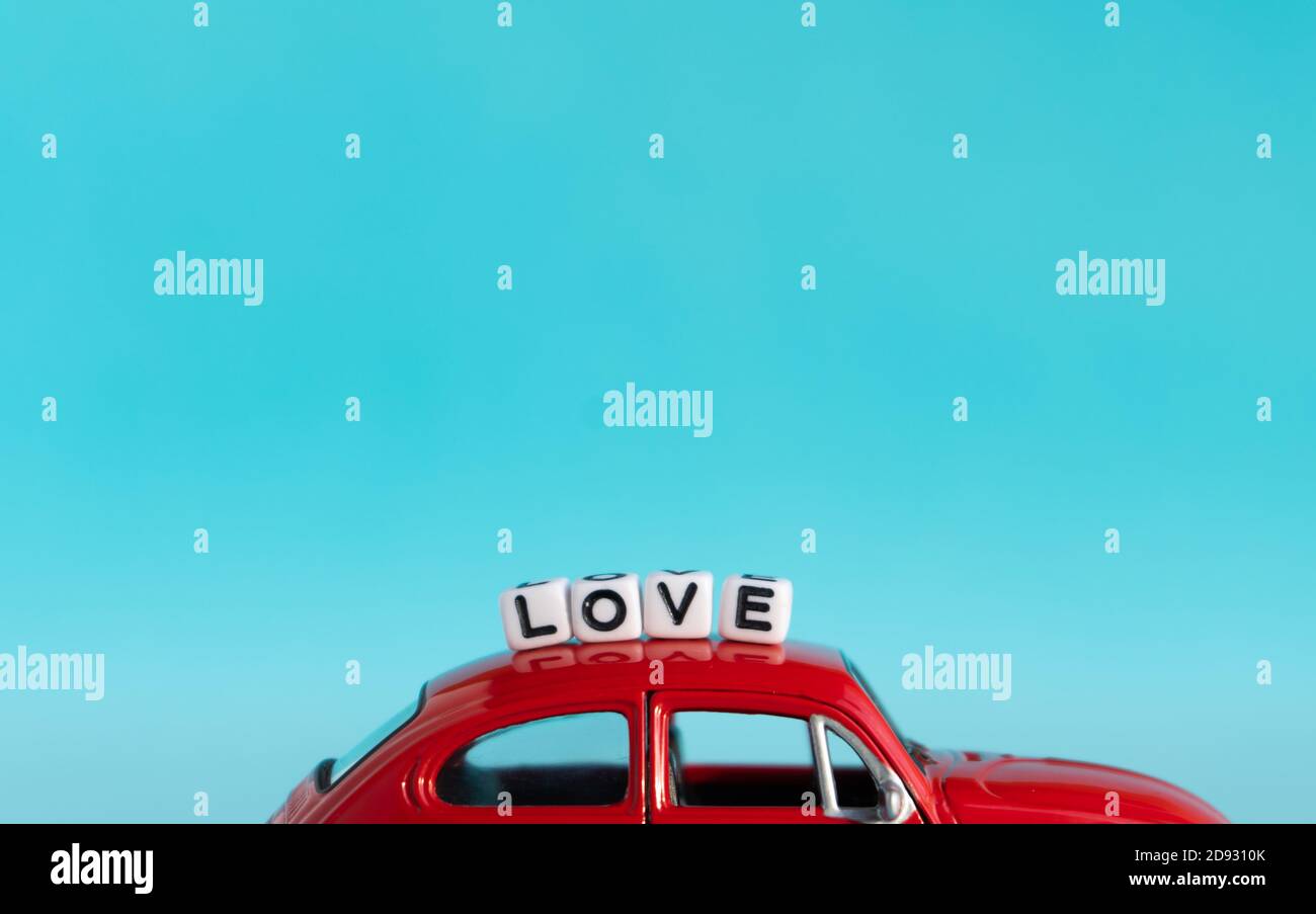 Perline lettera d'amore segno sulla parte superiore della piccola auto rossa su sfondo blu con spazio di copia. Design minimo. Foto Stock