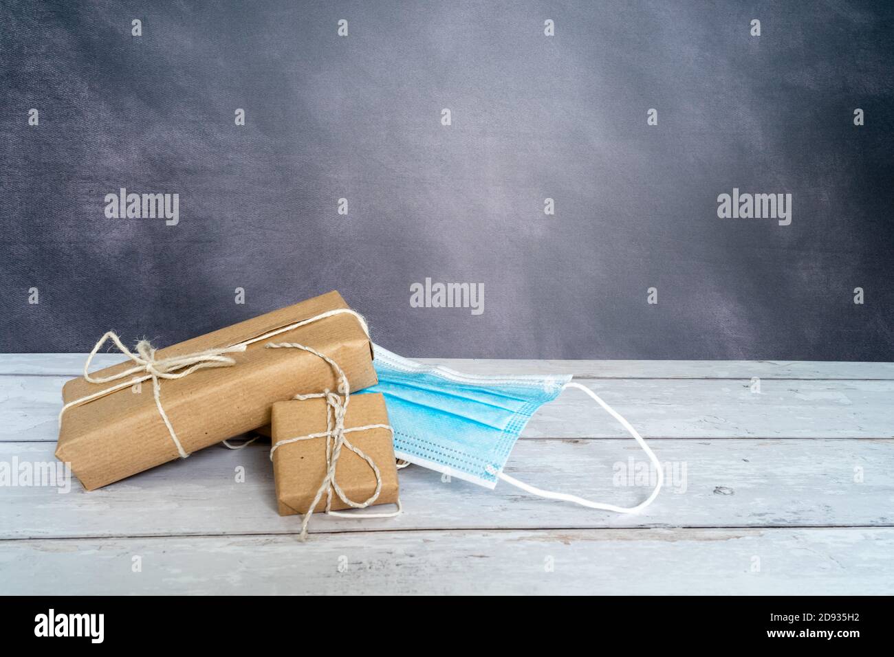 Natale e zero rifiuti, imballaggio eco-friendly. Regali avvolti in carta artigianale su un tavolo di legno su uno sfondo scuro. Maschera chirurgica sotto un po 'di dono. Foto Stock