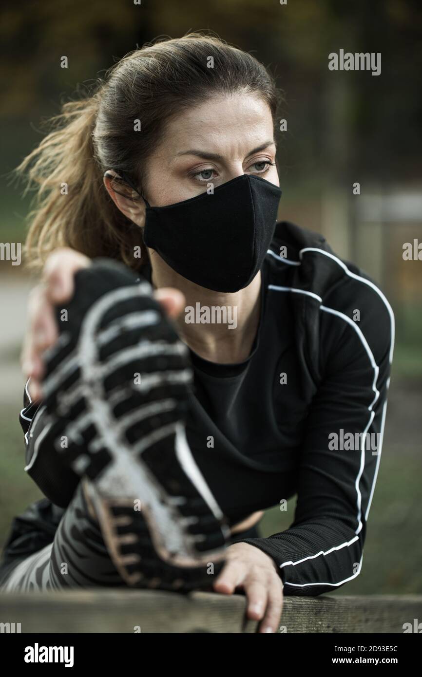 Donna con maschera nera che si esercita nel parco. Rimanere in buona salute durante l'epidemia di covid-19. Foto Stock