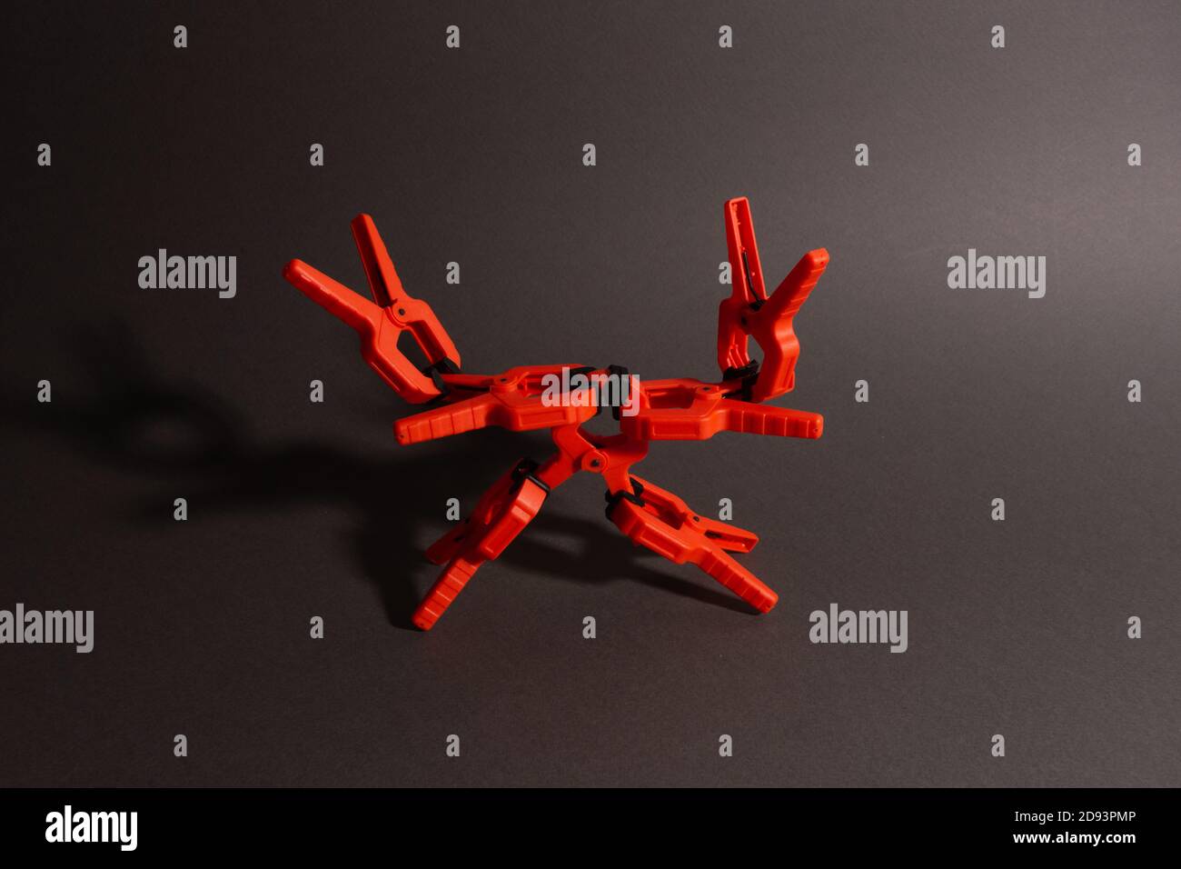 Stenditi, morsetti di carpenteria di colore arancio giacciono su un tavolo di legno. Una piramide a forma di robot costituito da morsetti. Foto Stock